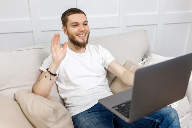 Jonge man thuis op de bank praten via video met een laptop