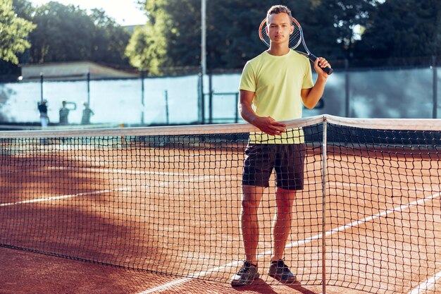 Jonge man tiener met tennisracket permanent in de buurt van net op gravel