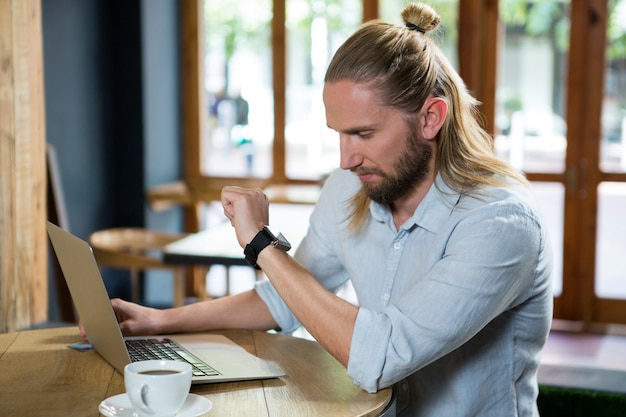 Jonge man tijd controleren zittend aan tafel in de coffeeshop