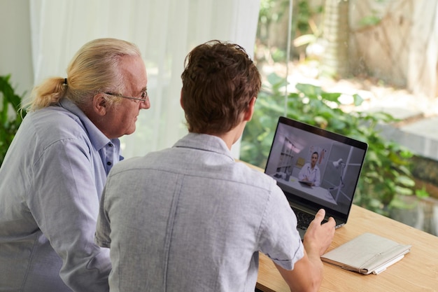 Jonge man toont zijn oudere vader hoe hij de telemedicine-dienst kan gebruiken