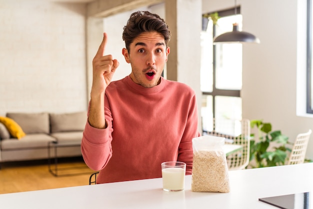 Jonge man van gemengd ras die havermout en melk eet als ontbijt in zijn keuken met een idee, inspiratieconcept.