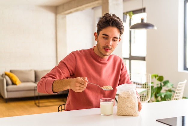 Jonge man van gemengd ras die havermout en melk eet als ontbijt in zijn keuken