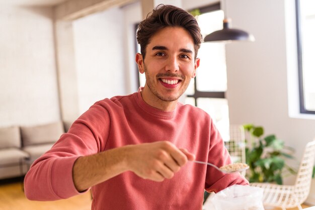 Jonge man van gemengd ras die havermout en melk eet als ontbijt in zijn keuken