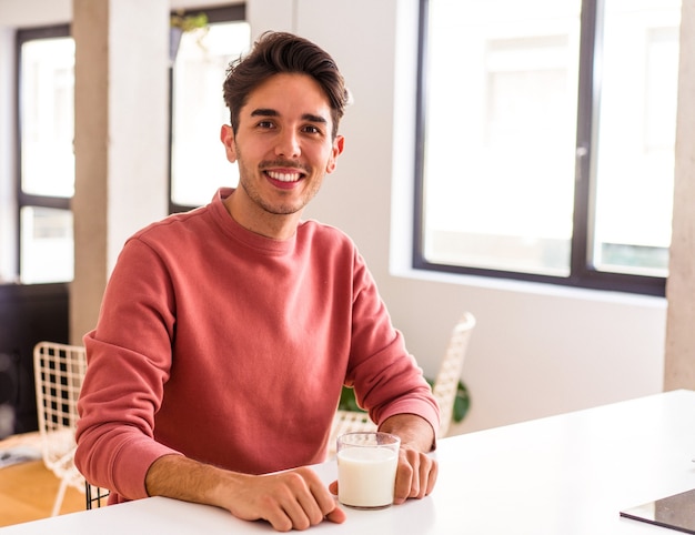 Jonge man van gemengd ras die melk drinkt als ontbijt