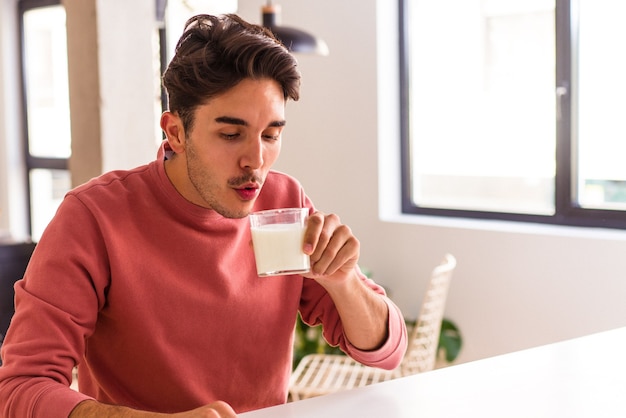 Jonge man van gemengd ras die melk drinkt voor het ontbijt.