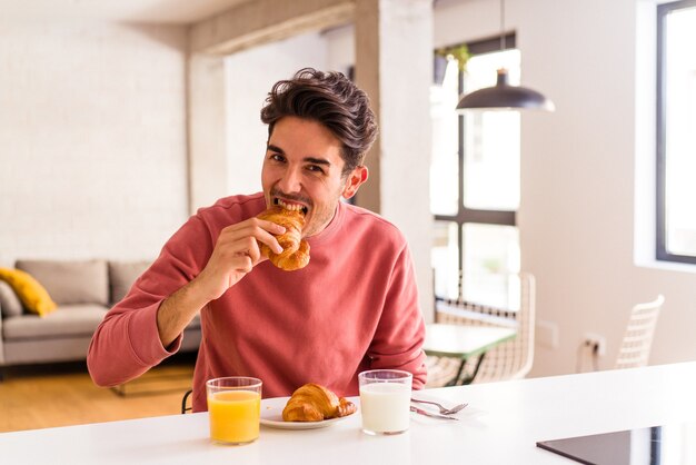 Jonge man van gemengd ras die 's ochtends croissants eet in een keuken