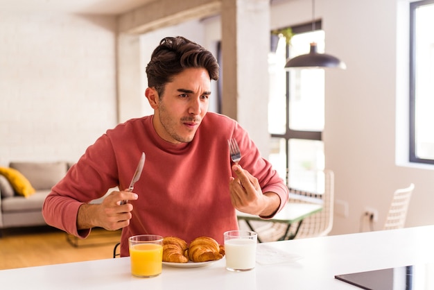 Jonge man van gemengd ras die 's ochtends croissants eet in een keuken