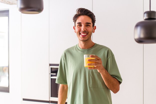 Jonge man van gemengd ras die sinaasappelsap drinkt in zijn keuken