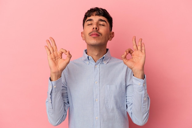 Jonge man van gemengd ras geïsoleerd op roze achtergrond ontspant na een zware werkdag die ze yoga uitvoert