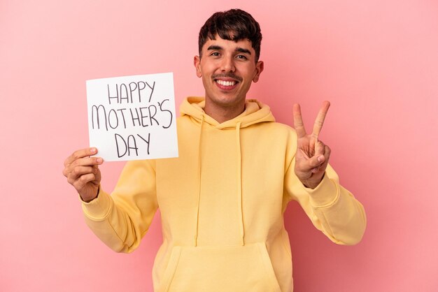 Jonge man van gemengd ras met een plakkaat voor gelukkige moederdag geïsoleerd op roze achtergrond