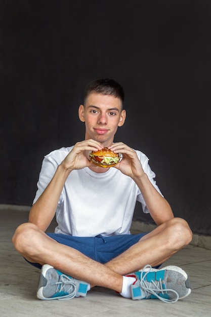 jonge man van tienerleeftijd zit op straat en eet hamburger