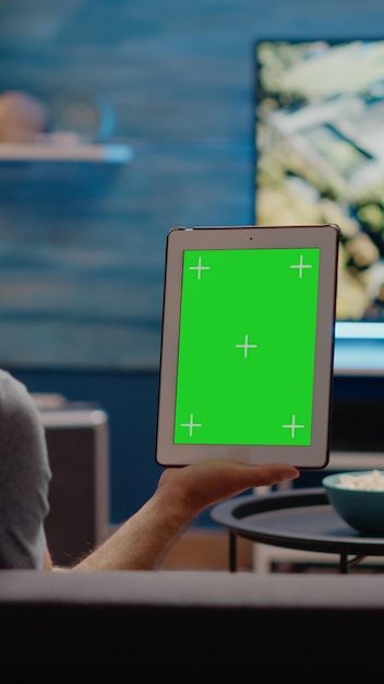 Jonge man verticaal met digitale tablet met groen schermontwerp in woonkamer. Moderne technologie voor chroma key gebruikt op mockup-sjabloon en geïsoleerde weergave voor kopieerruimte