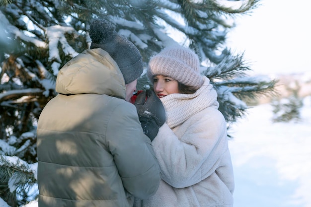 Jonge man verwarmt de handen van zijn geliefde met zijn adem Daten in park Verliefde paar in winterbos