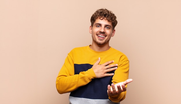 Jonge man voelt zich gelukkig en verliefd, glimlachend met de ene hand naast het hart en de andere naar voren gestrekt