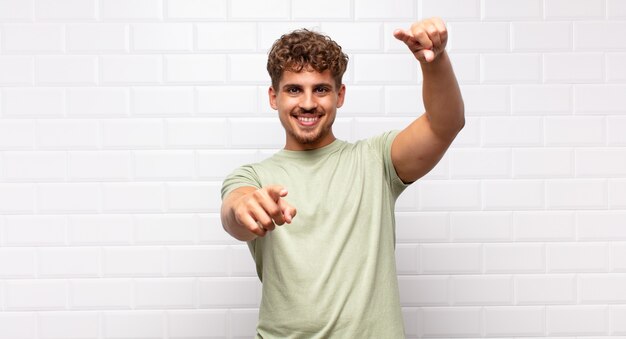 Jonge man voelt zich gelukkig en zelfverzekerd, wijst met beide handen naar voren en lacht, kiest jou