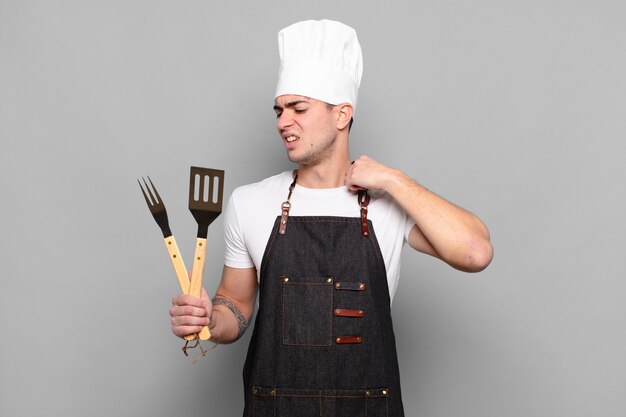 Jonge man voelt zich gestrest, angstig, moe en gefrustreerd, trekt aan de nek van het shirt, ziet er gefrustreerd uit met een probleem