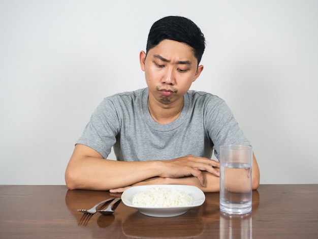 Jonge man voelt zich verveeld eten kijkend naar rijst en water aan tafel