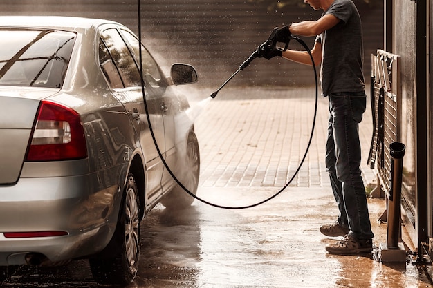 Jonge man wast een auto bij een selfservice carwash