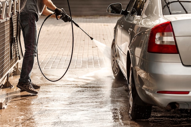 Jonge man wast een auto bij een selfservice carwash