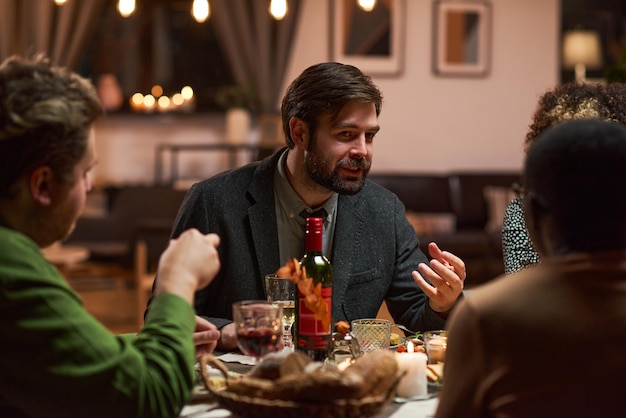 Jonge man zit aan de eettafel en praat met de mensen tijdens het etentje thuis