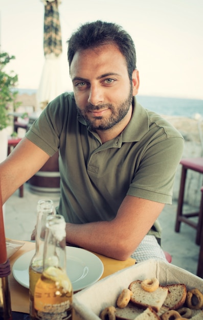 Jonge man zit aan het restaurant in de buurt van de zee.