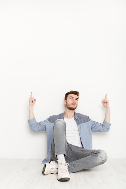 Jonge man zit en wijst naar boven met beide handen. knappe ontspannen man gebaren omhoog, geïsoleerd op een witte achtergrond