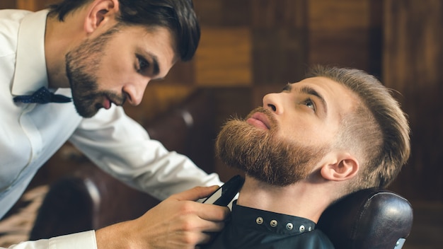 Jonge man zit in een kapperszaak terwijl kapper de baard trimt