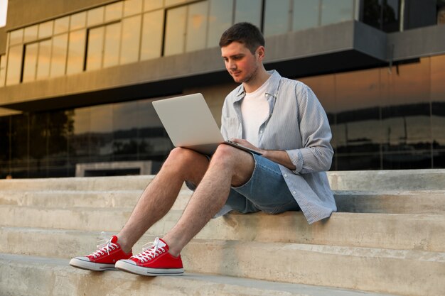 Jonge man zit in stappen en werkt in laptop buiten.