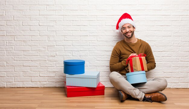 Jonge man zit met giften vieren Kerstmis kruising armen, glimlachen en ontspannen