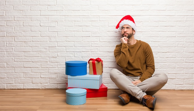 Jonge man zit met giften vieren Kerstmis twijfelen en verward