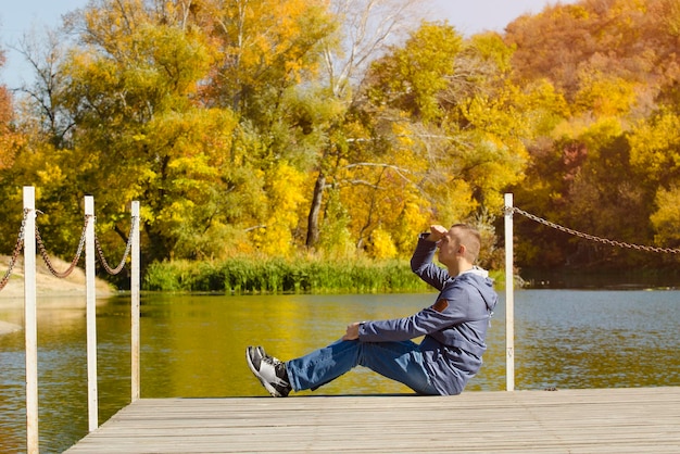 Jonge man zit op de pier Herfst zonnige dag Zijaanzicht