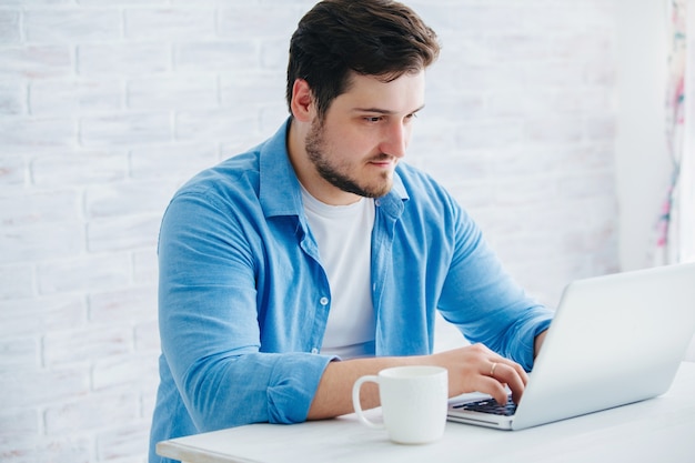 Jonge man zit op een laptop in de Studio met een kopje thee