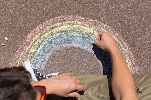 Jonge man zit op een stoep en tekent regenboog