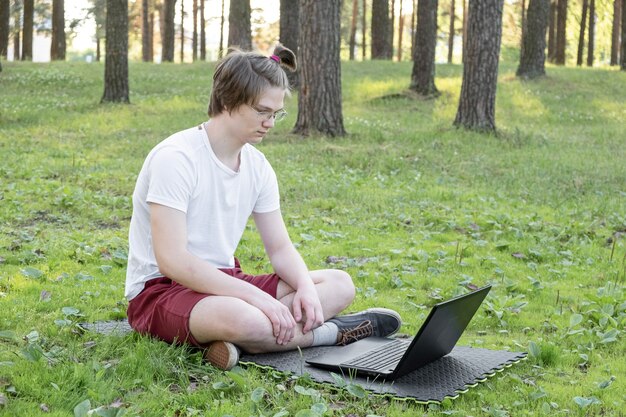 Jonge man zit op het gras in het park met zijn laptop