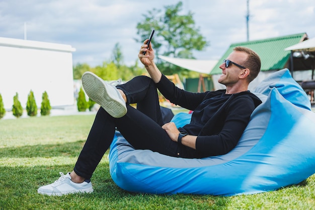 Jonge man zittend in een stoel buiten en praten aan de telefoon externe werk mannelijke freelancer