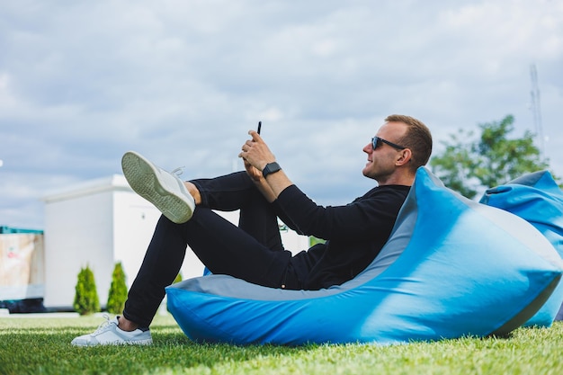 Jonge man zittend in een stoel buiten en praten aan de telefoon externe werk mannelijke freelancer