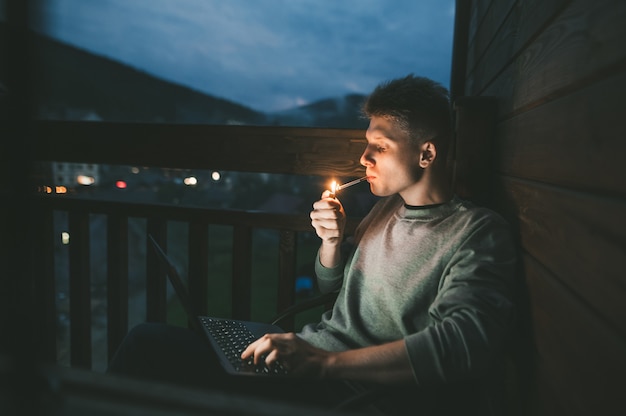 Foto jonge man zittend in een stoel op een balkon met behulp van een laptop