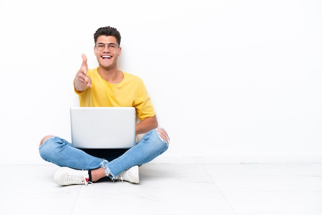 Jonge man zittend op de vloer geïsoleerd op een witte achtergrond handen schudden voor het sluiten van een goede deal