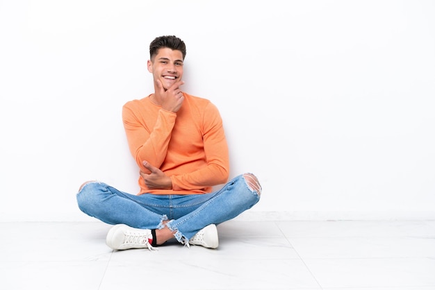Jonge man zittend op de vloer geïsoleerd op een witte achtergrond lachend