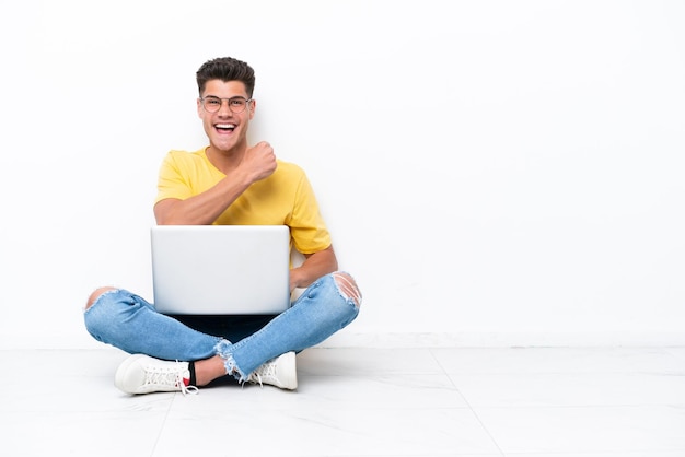 Jonge man zittend op de vloer geïsoleerd op een witte achtergrond vieren een overwinning