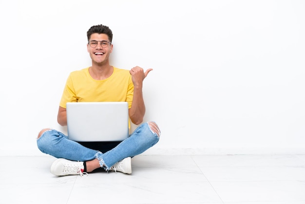 Jonge man zittend op de vloer geïsoleerd op een witte achtergrond wijzend naar de zijkant om een product te presenteren