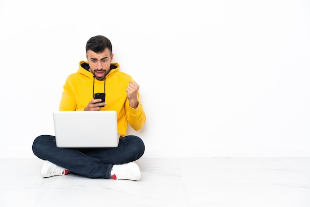 Jonge man zittend op de vloer met zijn laptop verrast en een bericht te sturen