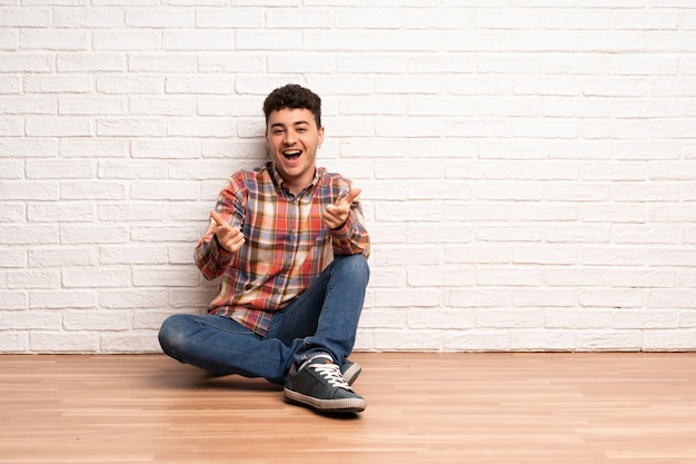 Jonge man zittend op de vloer naar voren wijzen en glimlachen