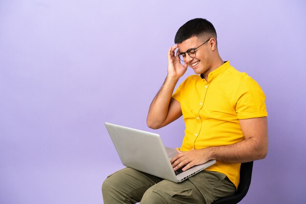 Jonge man zittend op een stoel met laptop aan het lachen