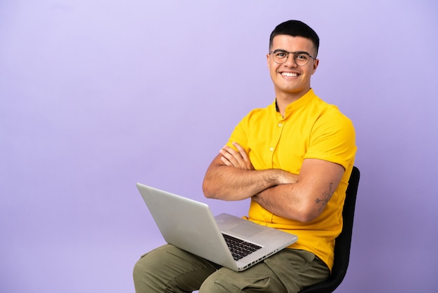 Jonge man zittend op een stoel met laptop met gekruiste armen en vooruitkijkend