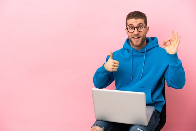 Jonge man zittend op een stoel met laptop met ok teken en duim omhoog gebaar