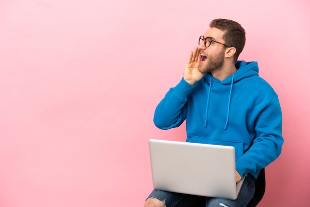 Jonge man zittend op een stoel met laptop schreeuwend met mond wijd open naar de zijkant