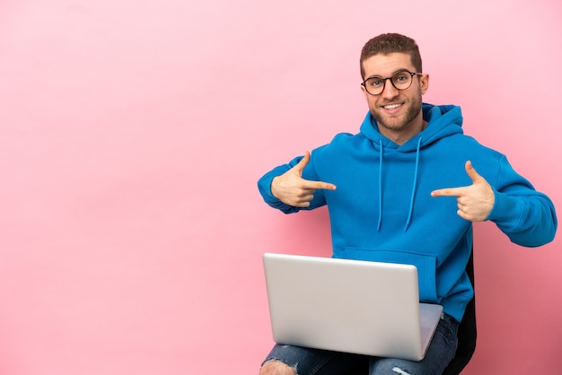 Jonge man zittend op een stoel met laptop trots en zelfvoldaan