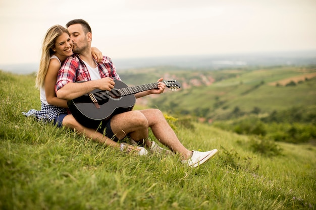 Jonge man zittend op het gras met zijn vriendin en gitaar spelen