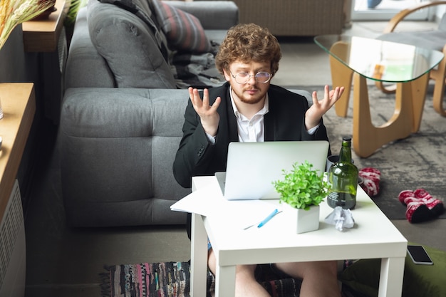 Jonge man zonder broek maar in jas aan het werk op een computer laptop op afstand kantoor tijdens coronavirus